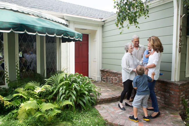 Старшая пара приветствует семью дома — стоковое фото