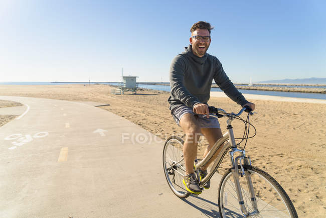 Молодой человек катается на велосипеде по дорожке на пляже — стоковое фото