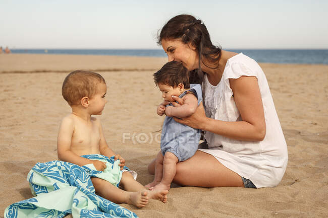 Mãe e bebês sentados na praia — Fotografia de Stock