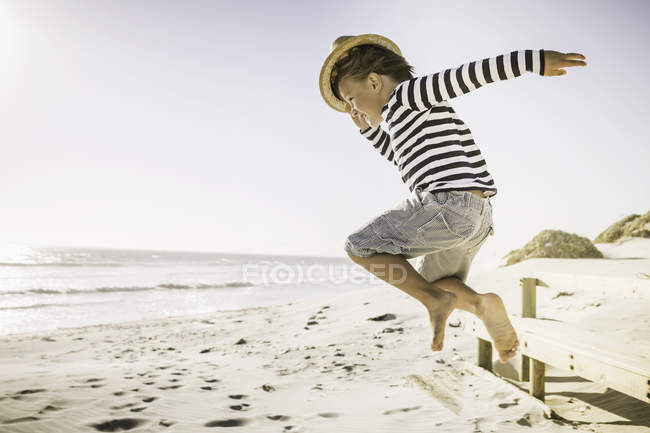 Young boy jumping on beach, wearing straw hat — Stock Photo