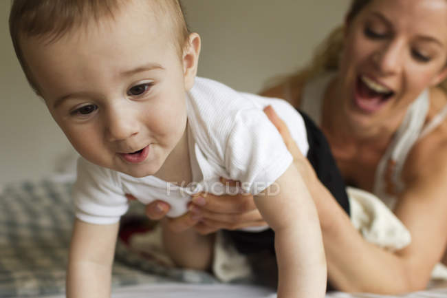 Mutter lenkt Baby, das auf Bett kriecht — Stockfoto