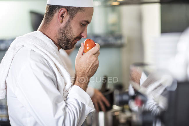 Шеф-повар нюхает помидор на кухне — стоковое фото