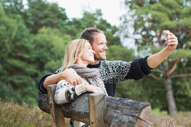 Mid adult couple on bench photographing themselves — Stock Photo