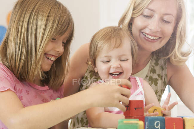 Grande sœur aidant bébé fille empiler blocs de construction souriant — Photo de stock