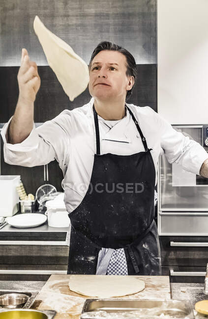 Шеф-повар бросает тесто для пиццы в воздух на коммерческую кухню — стоковое фото