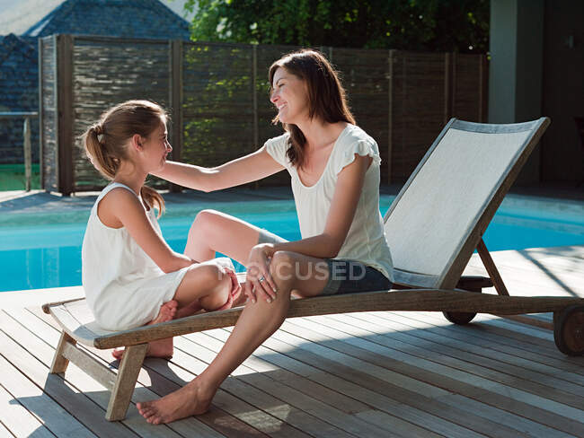 Girl and mother on lounge chair by swimming pool — Stock Photo