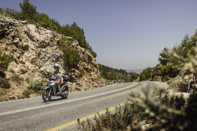 Mujer montando ciclomotor a lo largo de carretera de montaña en Samos, Grecia - foto de stock