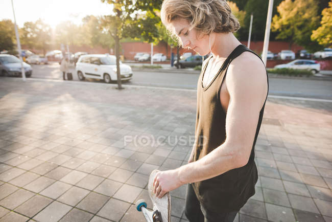 Young male urban skateboarder listening to earphone music on sidewalk — Stock Photo