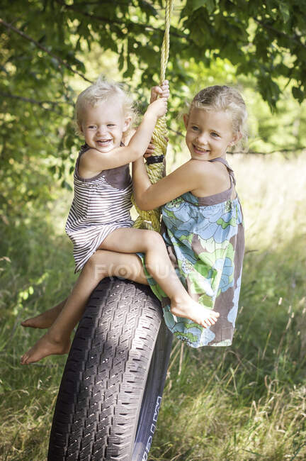 Female toddler and sister opposite each other playing on tire swing — Stock Photo