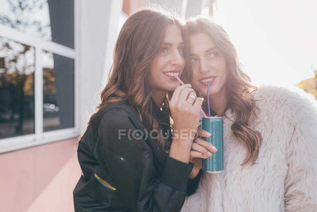 Twin sisters, outdoors, drinking can of soft drink with straws — Stock Photo