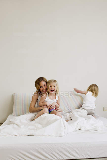 Retrato de mulher adulta média sentada na cama com duas filhas — Fotografia de Stock