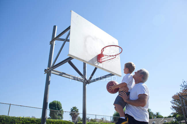 Чоловік піднімає онука до баскетбольного кільця — стокове фото