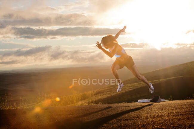 Young woman moving off starting blocks in rural setting — Stock Photo