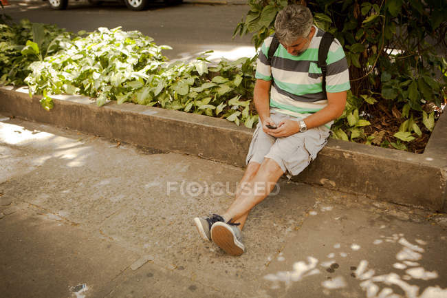 Зрелый мужчина, сидящий на тротуаре, пишет смс на смартфоне, Рио-де-Жанейро, Бразилия — стоковое фото