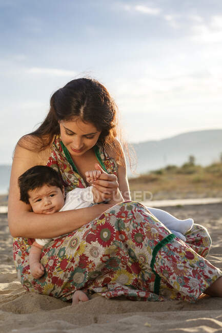 Мати сидить на піску, тримає дитину — стокове фото
