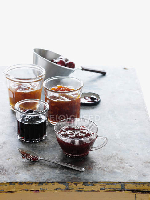 Macetas de vidrio de diferentes mermeladas de frutas en la mesa - foto de stock