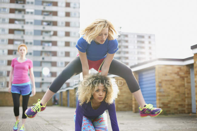 Three women exercising together wearing sports clothing and playing leap frog — Stock Photo