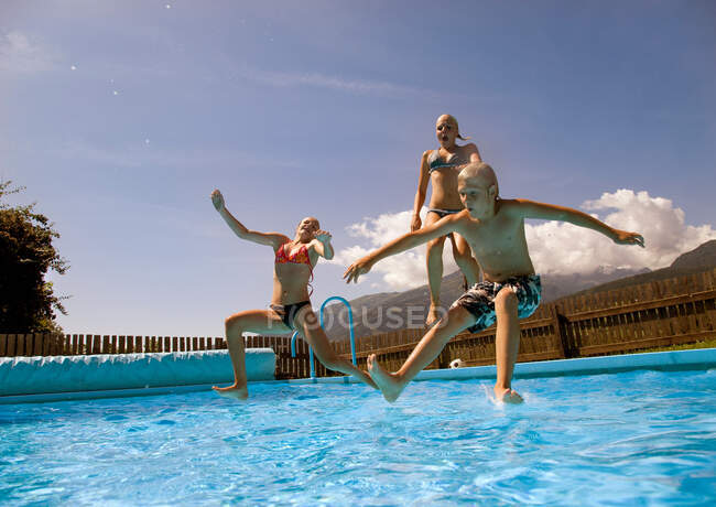 Chicas y chico saltando en la piscina - foto de stock
