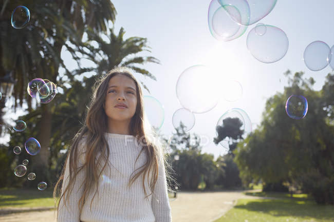 Girl in park surrounded by bubbles looking away — Stock Photo