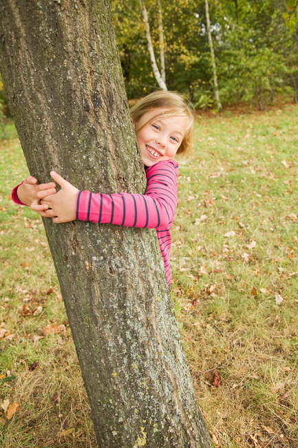 Smiling girl hugging tree outdoors — Stock Photo