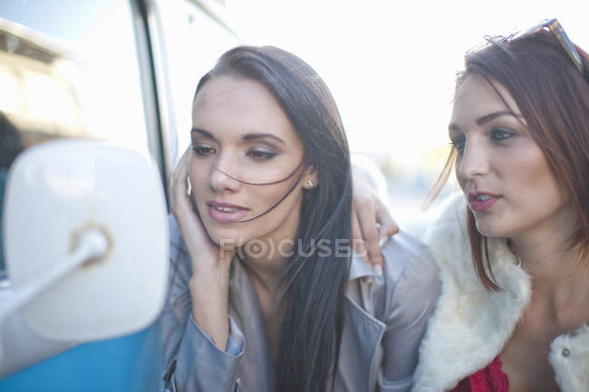 Two young adult female friends looking in camper van mirror — Stock Photo