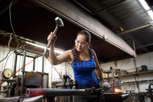 Female metalsmith hammering red hot metal rod on workshop anvil — Stock Photo