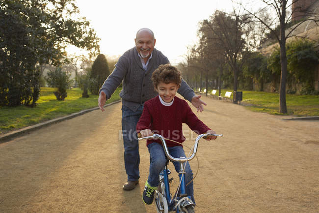 Abuelo enseñando a su nieto a montar en bicicleta en el parque - foto de stock