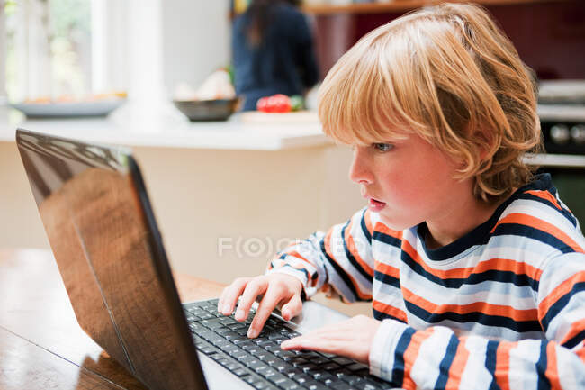 Мальчик смотрит на монитор ноутбука во время печати — стоковое фото