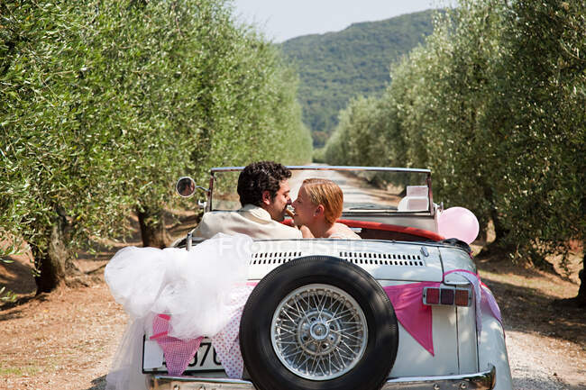 Recién casados besándose en coche clásico - foto de stock