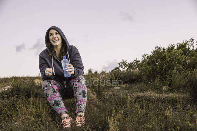 Pleine longueur vue de face de la femme portant capuche supérieure tenant bouteille d'eau regardant loin souriant — Photo de stock