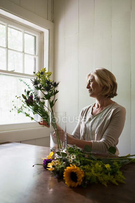 Зріла жінка розставляє квіти — стокове фото