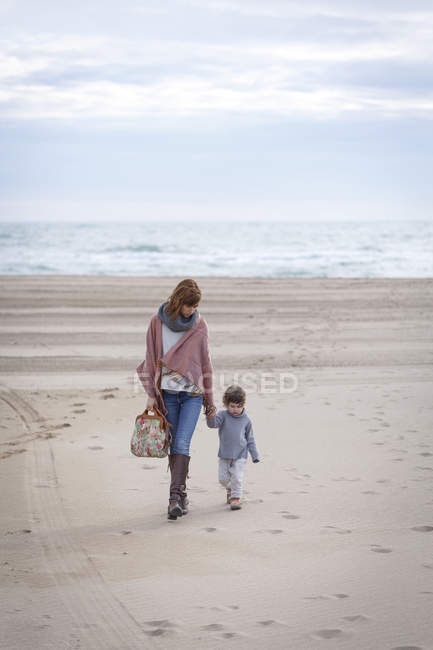 Madre e hija caminando por la playa cogidas de la mano - foto de stock
