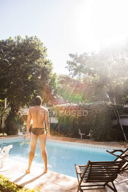 Visão traseira do homem em pé à luz do sol à beira da piscina — Fotografia de Stock