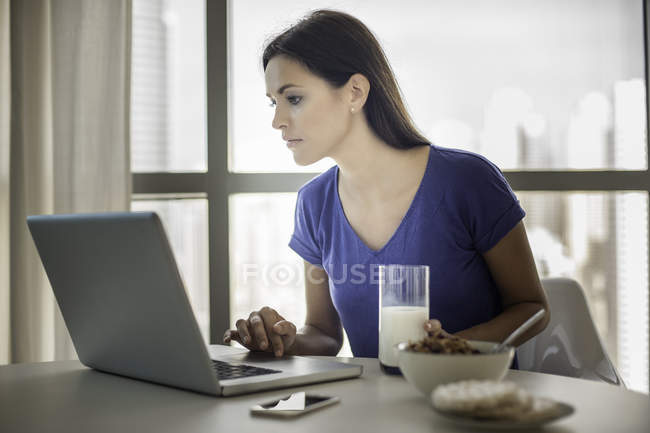 Молода жінка використовує ноутбук під час сніданку — стокове фото