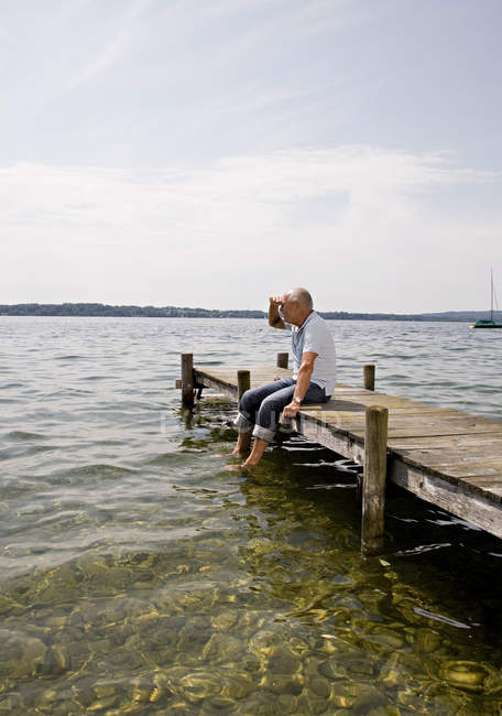 Senior man sitting on pier at lake — Stock Photo