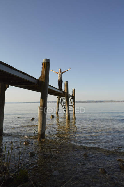 Woman on pier arms raised in yoga position — Stock Photo