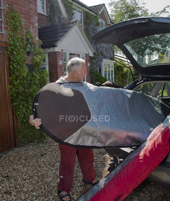 Старший человек загружает доску для серфинга в багажник автомобиля — стоковое фото