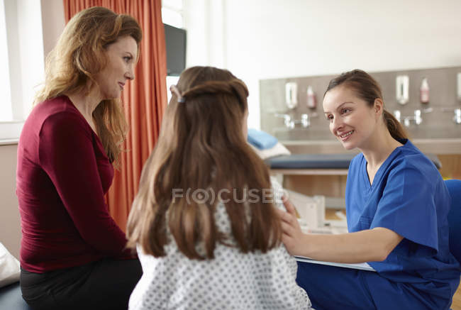 Enfermera hablando con paciente niña y madre - foto de stock
