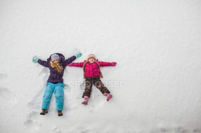 Due sorelle che giocano, facendo angeli di neve nella neve — Foto stock