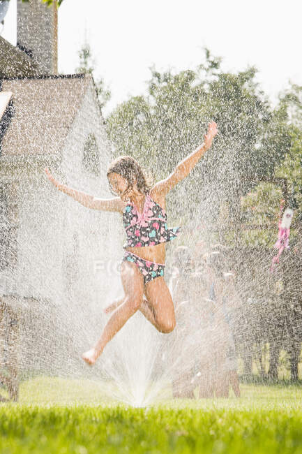 Girl jumping in sprinkler — Stock Photo
