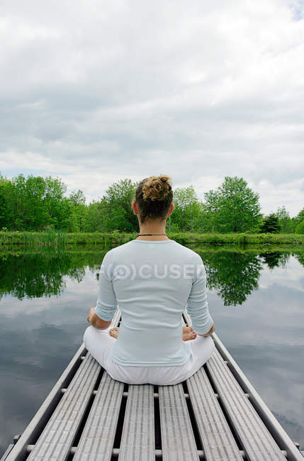 Visão traseira do homem meditando no cais de madeira — Fotografia de Stock