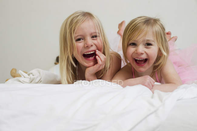 Portrait de deux petites soeurs blondes allongées devant au lit — Photo de stock