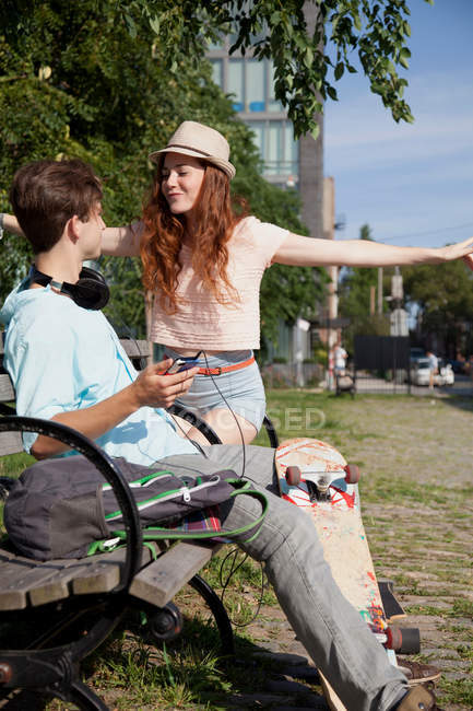 Jeune couple sur banc écoutant de la musique — Photo de stock