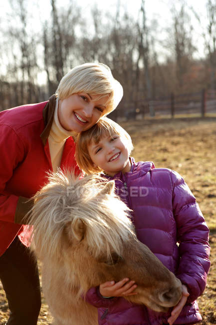 Retrato de madre e hija al aire libre, de pie con pony - foto de stock