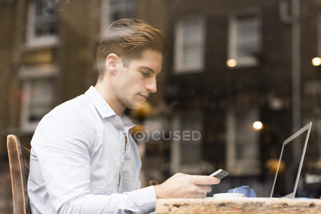 Window view of young businessman reading smartphone texts in cafe — Stock Photo