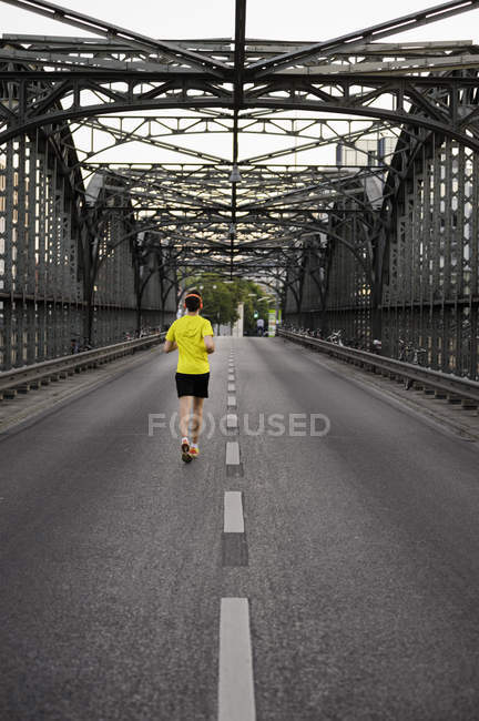 Вид ззаду молодого чоловіка спортсмена, що біжить через міст — стокове фото