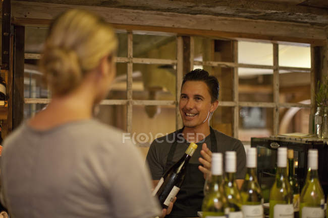 Sommelier sélectionnant parmi les bouteilles de vin pour cliente dans la boutique de vin — Photo de stock