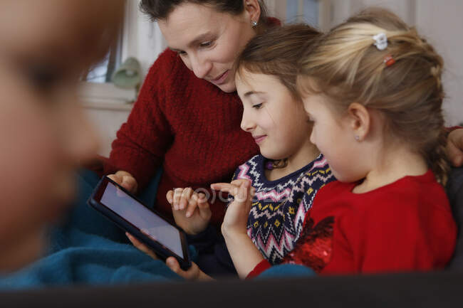 Madre e hijas en el sofá sentadas usando tableta digital sonriendo - foto de stock