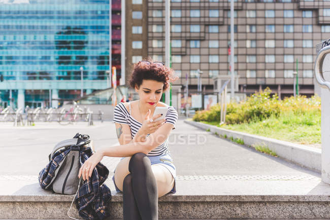 Mulher sentada na área urbana de mensagens de texto no smartphone, Milão, Itália — Fotografia de Stock