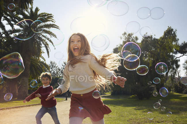Girl and boy in park running after bubbles — Stock Photo